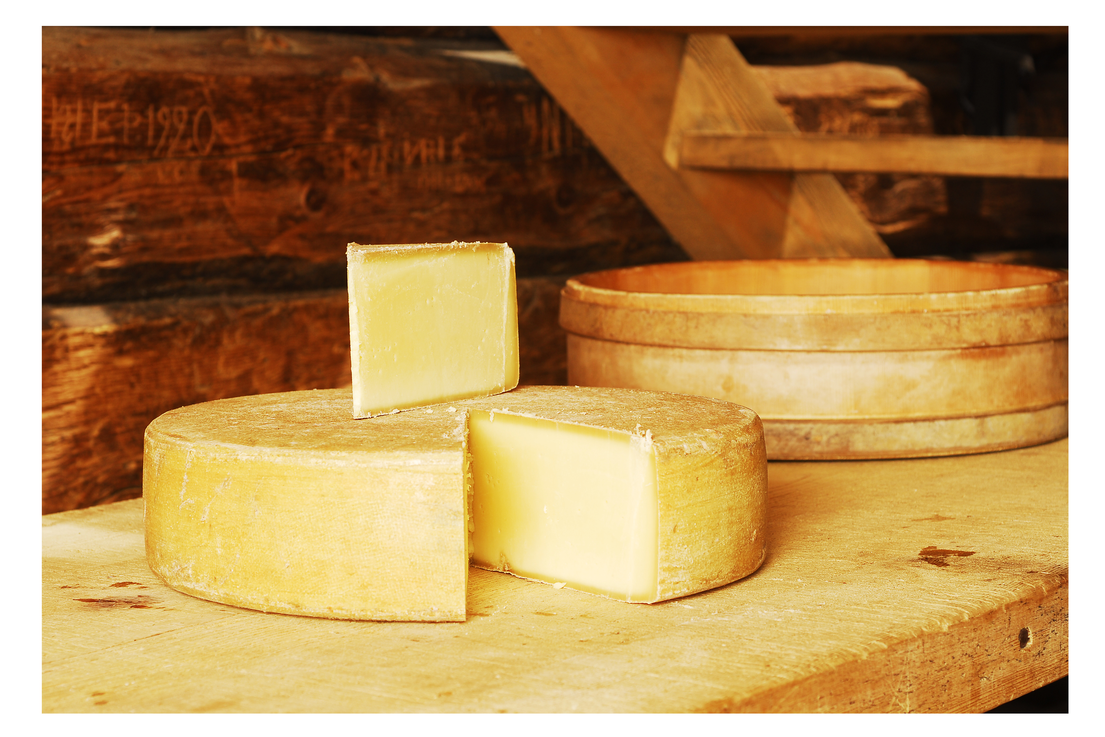 Aufgeschnittener Laib Bergkäse mit einer Holzgepse danebben